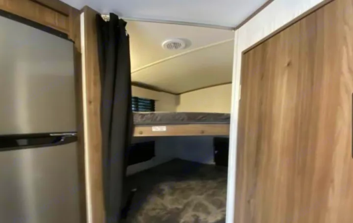 Inside this RV rental, a cozy bunk room with an upper bed is visible from the main area, next to the fridge. Perfect for trips.. Cruiser RV MPG 2023