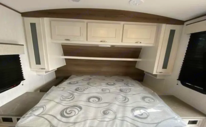 Spacious RV rental bedroom features a comfortable bed, ample overhead storage, and side cabinets, ideal for your travels.. Cruiser RV MPG 2023