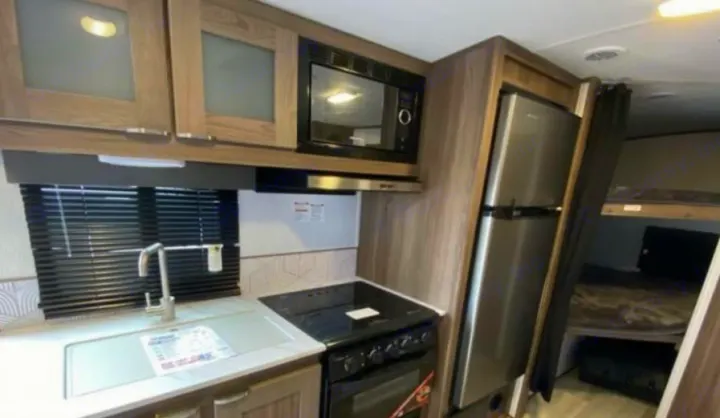Modern RV rental kitchen with microwave, stove, sink, and fridge. Adjacent area includes bunk beds. Explore comfortable travel!. Cruiser RV MPG 2023