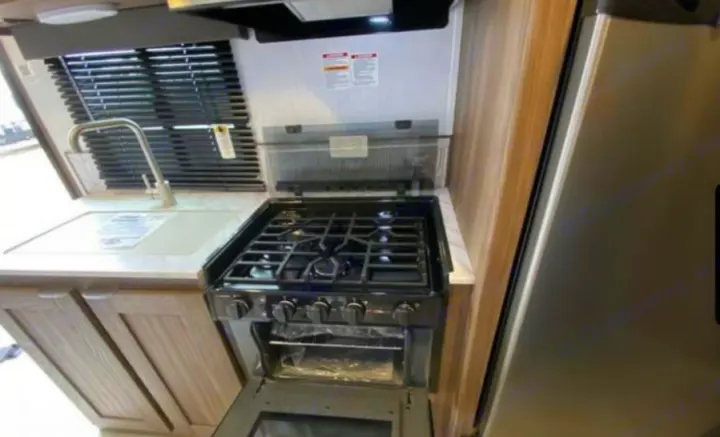 Inside an RV rental: a compact kitchen featuring a sink, window blinds, three-burner stovetop with oven, and stainless fridge.. Cruiser RV MPG 2023