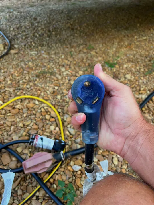 Close-up of a hand holding a 30A 125V RV electrical plug, crucial for rv rental power hookups at campsites.. Dutchmen Aspen Trail 2023