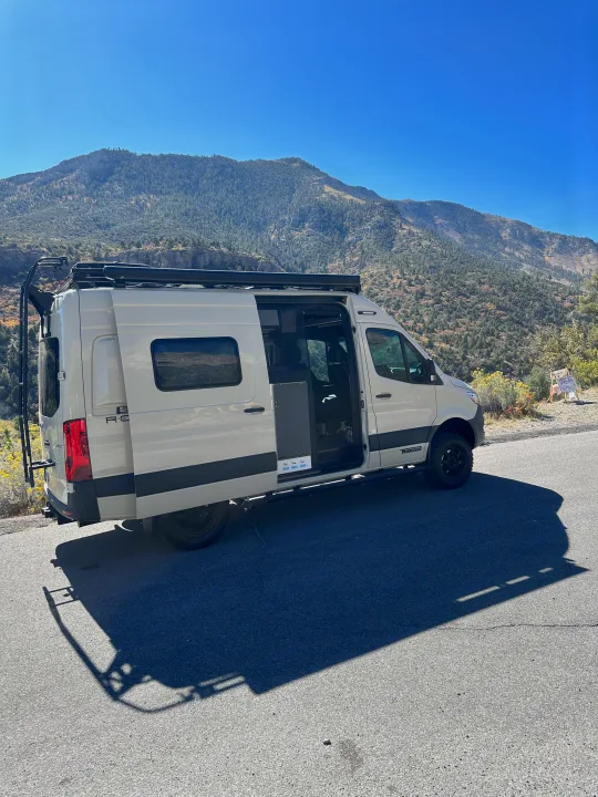 White camper van RV rental parked on a scenic mountain road with doors open. Perfect for an outdoor adventure trip.. Mercedes Revel 2024