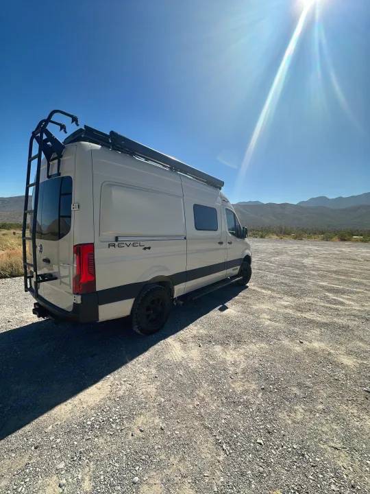 RV rental: Winnebago Revel 4x4 camper van parked on gravel, ready for adventure under a bright, sunny sky with mountains.. Mercedes Revel 2024