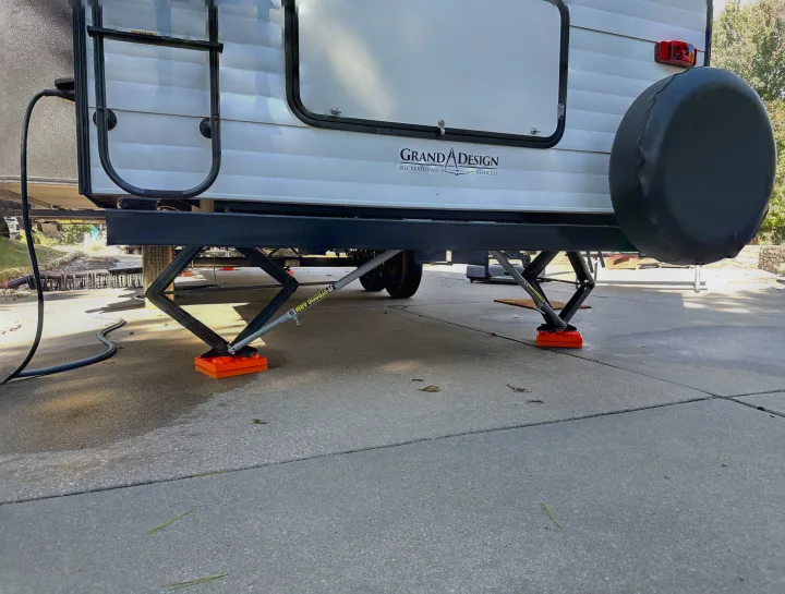 Back of a Grand Design RV rental, stabilized on concrete. Shows rear jacks on orange pads and power connection.. Grand Design Transcend Xplor 2022