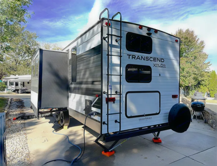 RV rental: Rear view of a white Grand Design Transcend Xplor travel trailer parked with slide-out extended and hookups connected.. Grand Design Transcend Xplor 2022