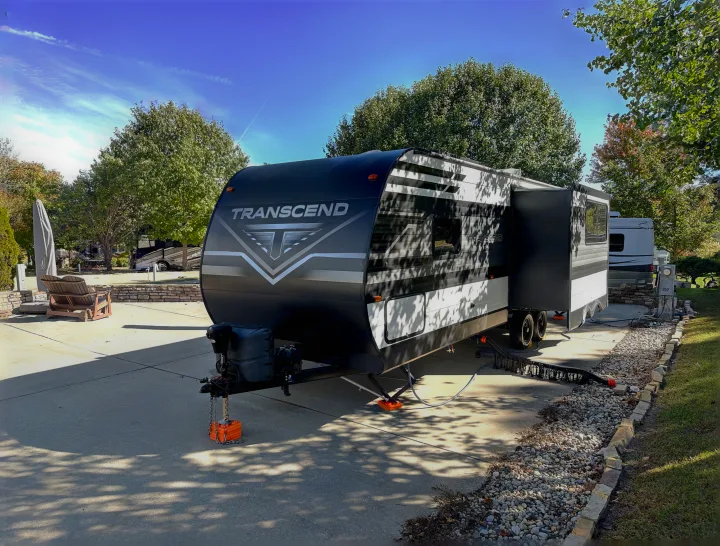 A modern black & white Transcend travel trailer, likely an rv rental, parked on a concrete pad with utilities at a sunny RV park.. Grand Design Transcend Xplor 2022