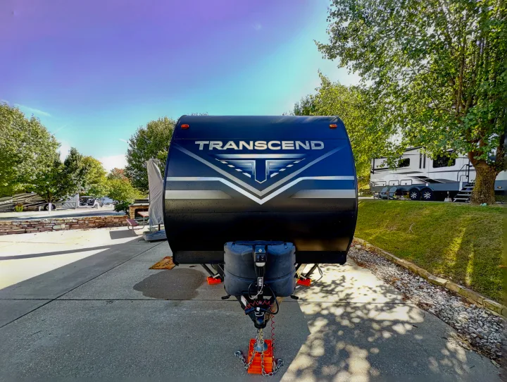 A black Transcend travel trailer, an RV rental, securely parked on concrete at a sunny campsite, ready for adventure.. Grand Design Transcend Xplor 2022