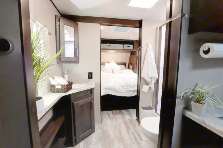 This RV rental interior showcases a modern bathroom with vanity, sink, and toilet, connecting to a comfortable bedroom.. Grand Design Transcend Xplor 2022