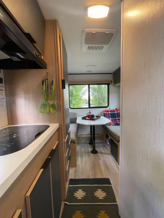 RV rental's modern interior: kitchen cooktop & utensils, dining area with table, benches, and window.. Cruiser RV Hitch 16RD 2022