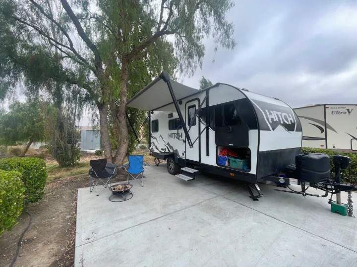 RV rental setup: A modern Hitch travel trailer parked at a campsite, with an extended awning, fire pit, and chairs.. Cruiser RV Hitch 16RD 2022