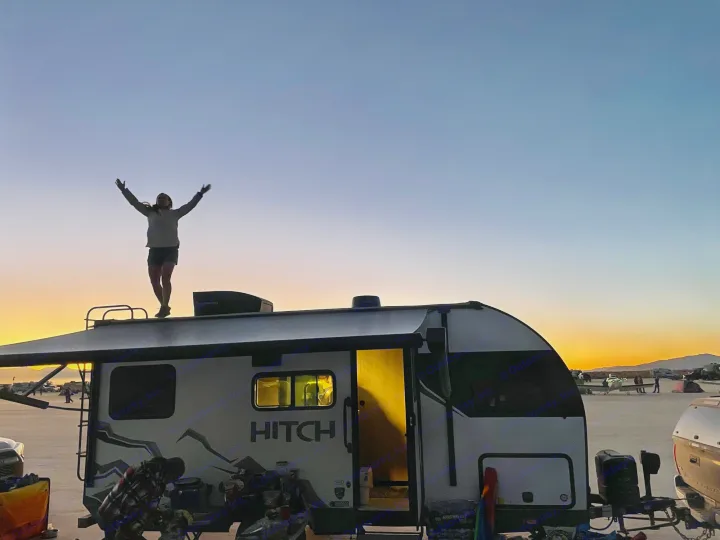 A person in silhouette stands triumphantly on an rv rental's roof, arms raised against a stunning sunset sky.. Cruiser RV Hitch 16RD 2022