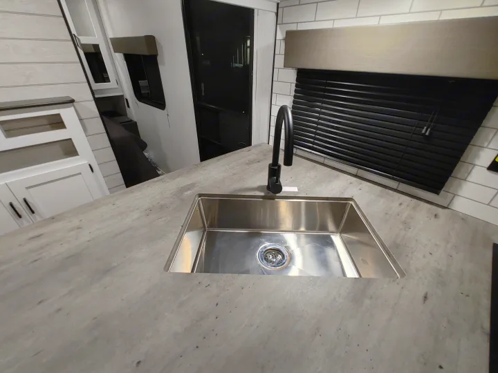Inside an RV rental: a modern kitchen with a stainless steel sink, black faucet, and patterned gray countertop.. Keystone RV Hideout 2023