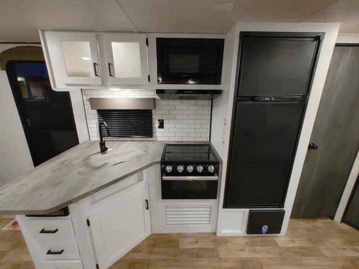 Modern RV rental kitchen featuring white cabinets, black appliances, sink, and stylish subway tile backsplash. Spacious counter.. Keystone RV Hideout 2023