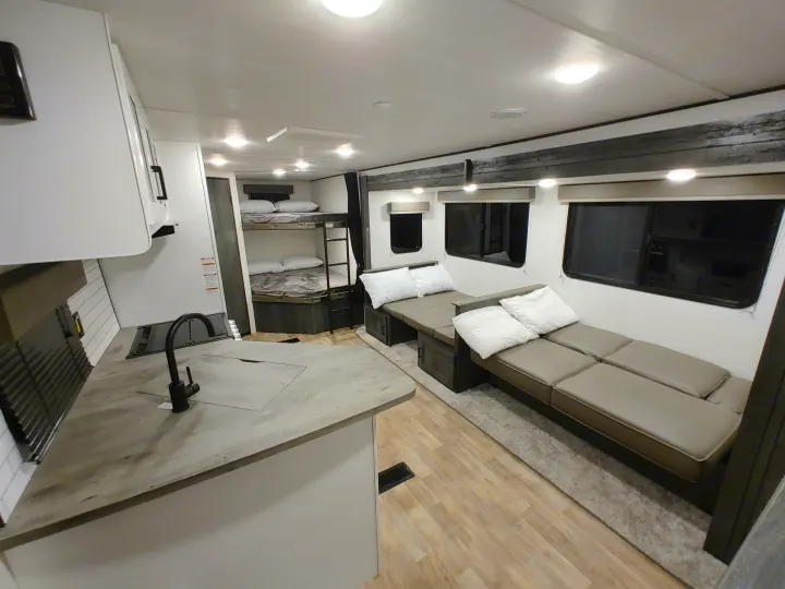 Spacious RV rental interior with a modern kitchen, cozy bunk beds, and a convertible lounge.. Keystone RV Hideout 2023