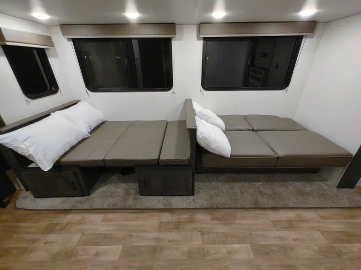 RV rental interior showcasing two convertible bench seats with pillows, windows, and overhead lights. Cozy and functional.. Keystone RV Hideout 2023