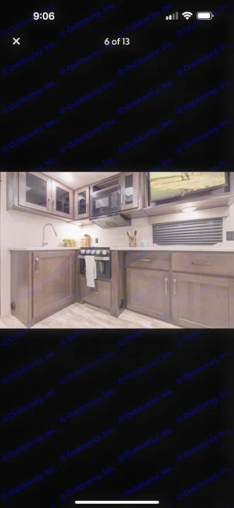 Modern RV rental kitchen: dark wood cabinets, countertop, sink, microwave, stove, and TV. Perfect for road trips.. Grand Design Transcend Xplor 2021