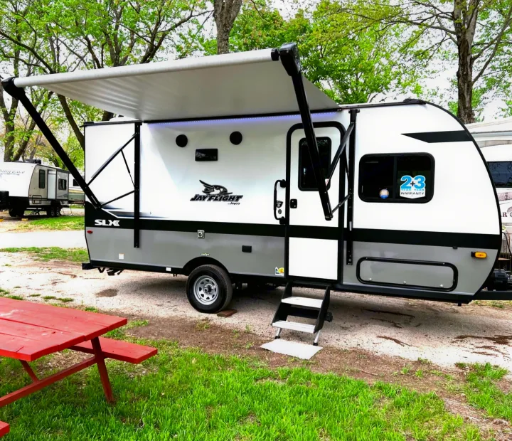 This RV rental, a Jay Flight SLX travel trailer, is set up at a campground with its awning extended and a red picnic table nearby.. Jayco Jay Flight 2023