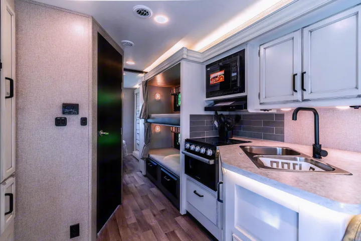 Modern RV rental interior with a well-equipped kitchen (sink, stove, microwave) and comfortable bunk beds for travel comfort.. Jayco Redhawk 2022