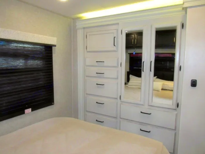 RV rental bedroom interior with a built-in wardrobe, drawers, and mirrors opposite a bed. Compact and functional design.. Jayco Redhawk 2022