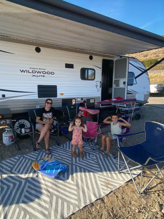 Family enjoying their Forest River Wildwood X-Lite RV rental at a sunny campsite with outdoor seating and grill.. Forest River Wildwood X-Lite 2018