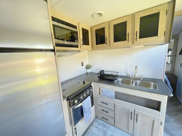 Modern RV rental kitchen with stainless steel appliances, dual sink, ample storage, and stylish light wood cabinets.. Heartland RVs Prowler 2022