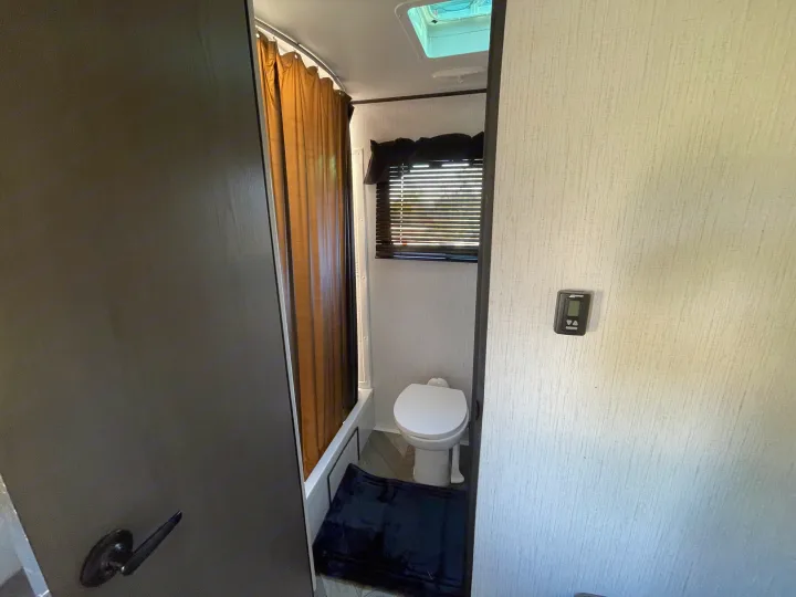 Compact RV rental bathroom features a toilet, shower with curtain, and a window for comfortable travel.. Heartland RVs Prowler 2022