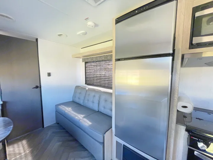 Modern RV rental interior: Features a compact kitchen with fridge, microwave, stove, and a comfy sofa.. Heartland RVs Prowler 2022