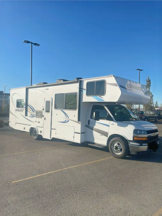 A white Conquest motorhome, perfect for an RV rental, parked on asphalt under a clear blue sky.. Gulf Stream Conquest 2020