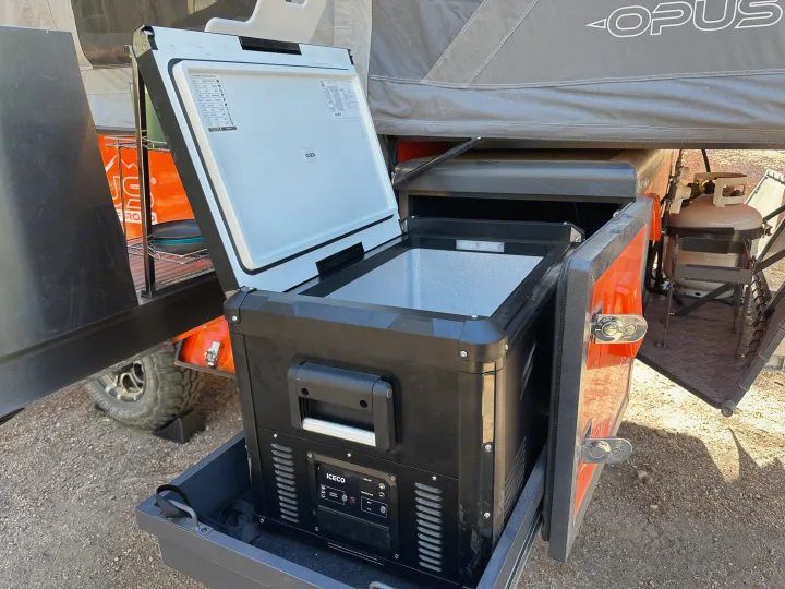 RV rental's pull-out outdoor kitchen featuring an open Iceco portable fridge, ideal for easy access on camping trips.. Opus Camper Opus Camper Popup Trailer 2023