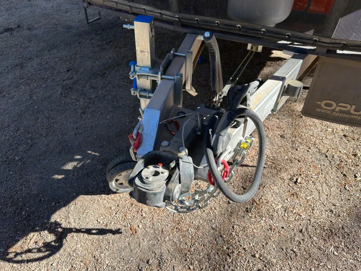 RV rental trailer's coupler, safety chains, and electrical connections. Jockey wheel visible on gravel.. Opus Camper Opus Camper Popup Trailer 2023