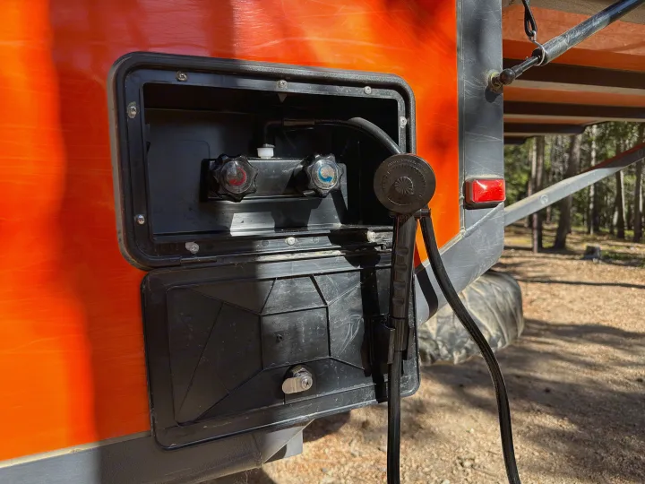 Outdoor shower setup on an orange RV rental. Features hot/cold taps, hose, and shower head for campsite use.. Opus Camper Opus Camper Popup Trailer 2023