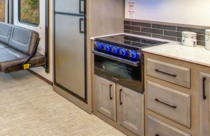 Inside this modern rv rental, a compact kitchen with a stove, fridge, and a stylish fold-down bench maximizes space.. Heartland Fuel F-265 2022