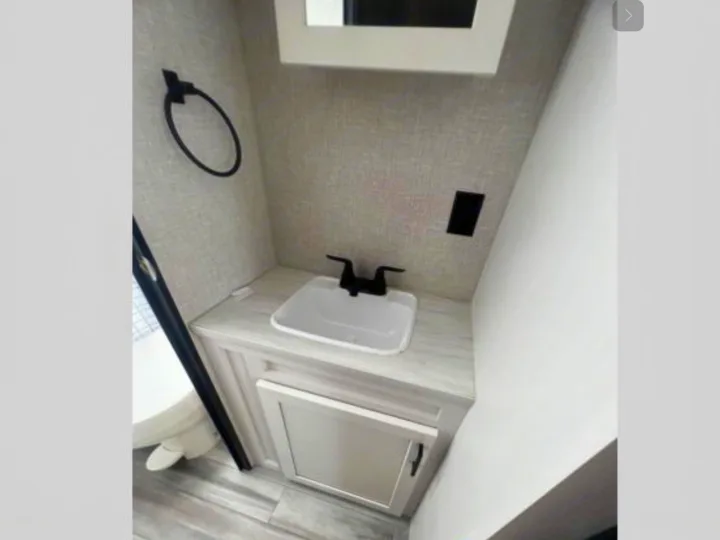 Compact RV rental bathroom featuring a modern sink, black faucet, and light vanity with storage.. Jayco Jay Flight 264BH 2024
