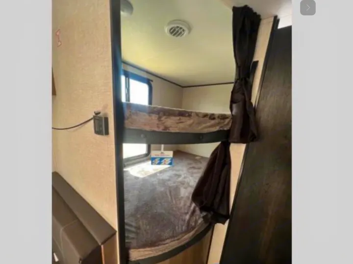Inside an RV rental: comfortable bunk beds with a window, a control panel, and dark privacy curtains.. Jayco Jay Flight 264BH 2024