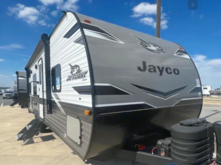 A grey and white Jayco Jay Flight travel trailer, ideal for an rv rental, is parked outdoors in a lot.. Jayco Jay Flight 264BH 2024