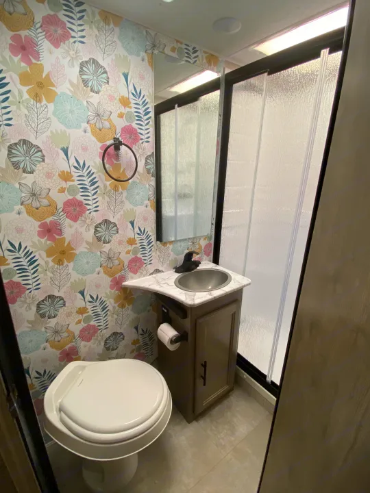 A colorful floral wallpaper brightens this RV rental bathroom with a compact sink, toilet, and shower stall.. Forest River Coachmen Freelander Premier 2022