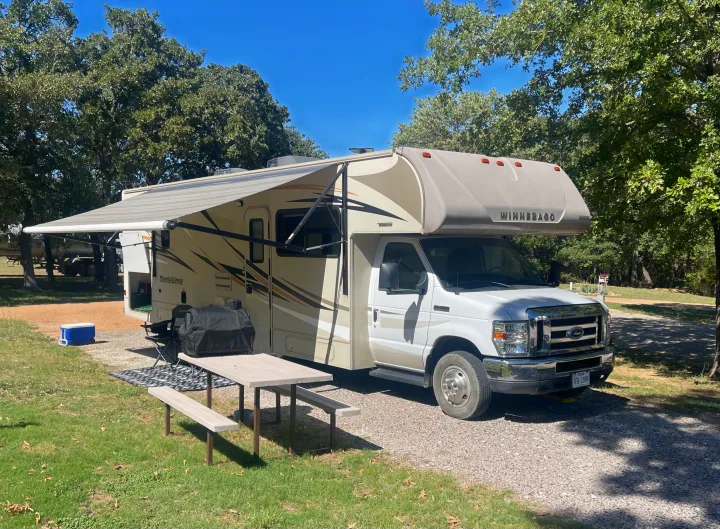 Winnebago Minnie Winnie RV rental setup at a shaded park campsite with picnic table & awning, ideal for outdoor recreation.. Winnebago Minnie Winnie 2019