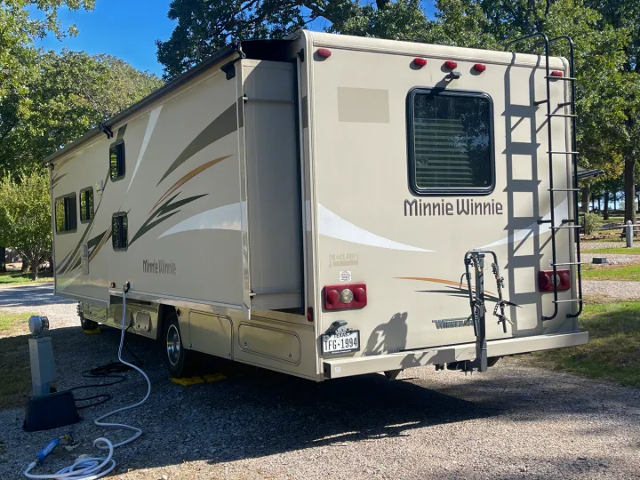 This Winnebago Minnie Winnie rv rental is set up at a sunny campsite with its slide-out extended and hookups connected.. Winnebago Minnie Winnie 2019