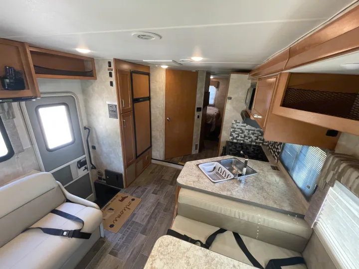 Spacious RV rental interior features a full kitchen with sink, comfortable seating with seatbelts, and a glimpse of the bedroom.. Winnebago Minnie Winnie 2019