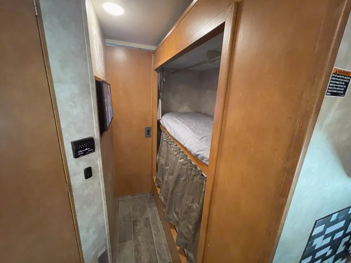 RV rental interior: a narrow hallway leading to bunk beds with a privacy curtain, plus a wall-mounted TV and control panel.. Winnebago Minnie Winnie 2019