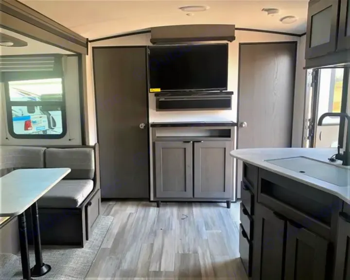 Gray RV rental interior: dining booth, central TV, and a kitchen island with sink on the right.. Cruiser RV MPG Ultra Lite 2022