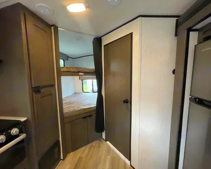 RV rental interior: dark wood cabinets, light walls, bunk beds, kitchen area, and a private room door.. Cruiser RV MPG Ultra Lite 2022
