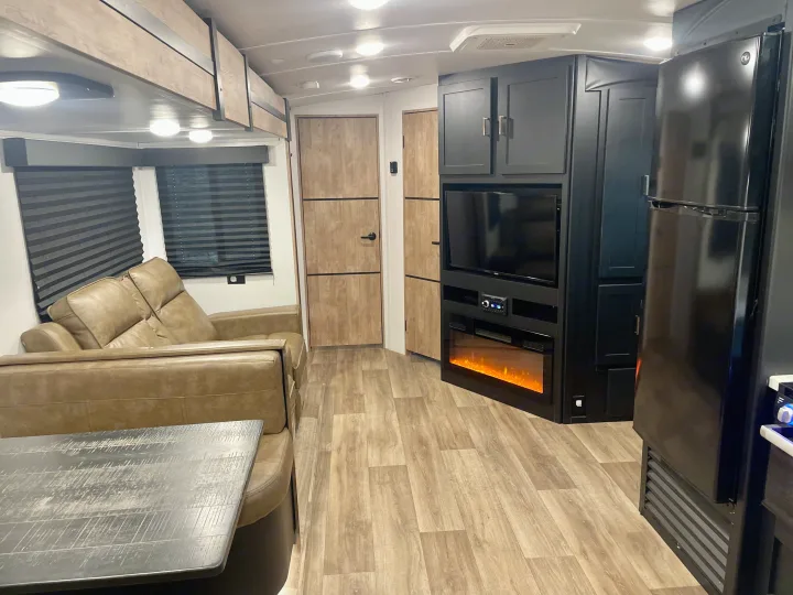 Bright RV rental living space with tan sofa, TV, electric fireplace, and dark cabinets. Modern interior design.. Keystone Outback 2022