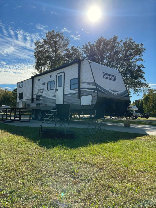 Coleman RV rental at a sunny campsite with chairs, table, and fire pit. Perfect for outdoor adventures!. Dutchmen Coleman Lantern 2019