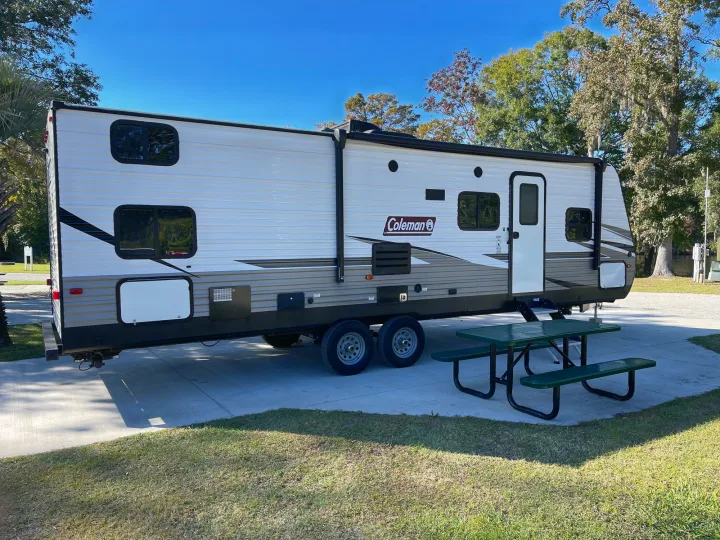 White Coleman RV rental parked at a sunny campground with a green picnic table, ready for outdoor adventure.. Dutchmen Coleman Lantern 2019