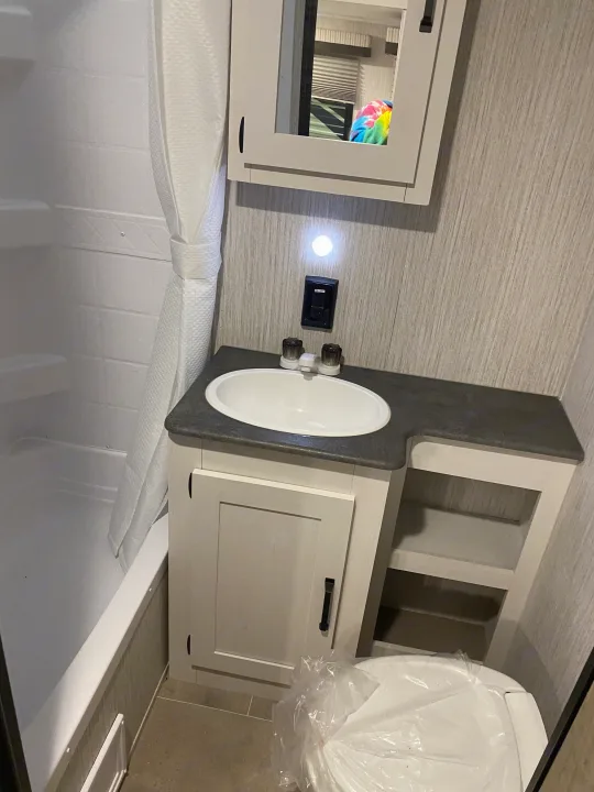 This RV rental bathroom features a compact shower/tub, sink vanity, and a plastic-covered toilet.. Forest River Palomino Puma XLE Lite 2021