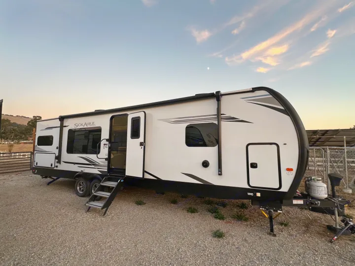 White Solaire travel trailer RV rental parked on gravel at dusk, with moon and hills. Perfect for your next adventure.. Palomino Salaire Ultralite 2022