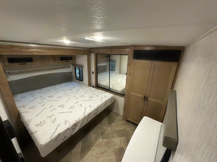 Comfortable RV rental bedroom with a bamboo mattress, overhead cabinets, and mirrored closet, showing compact RV living.. Palomino Salaire Ultralite 2022