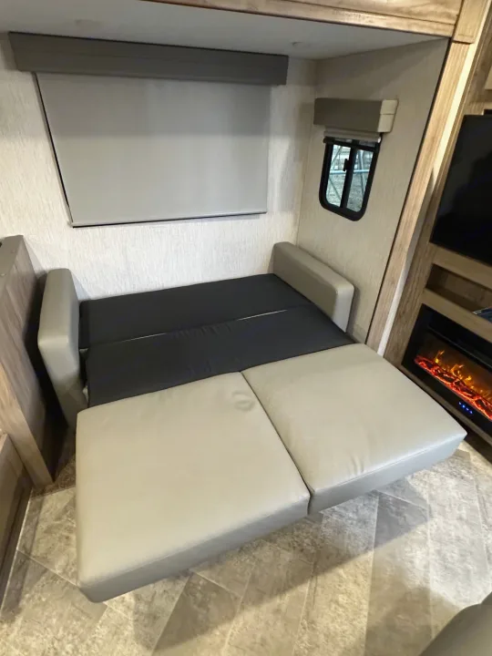 RV rental featuring a grey & black convertible sofa bed, large window, and cozy fireplace in a compact interior.. Palomino Salaire Ultralite 2022
