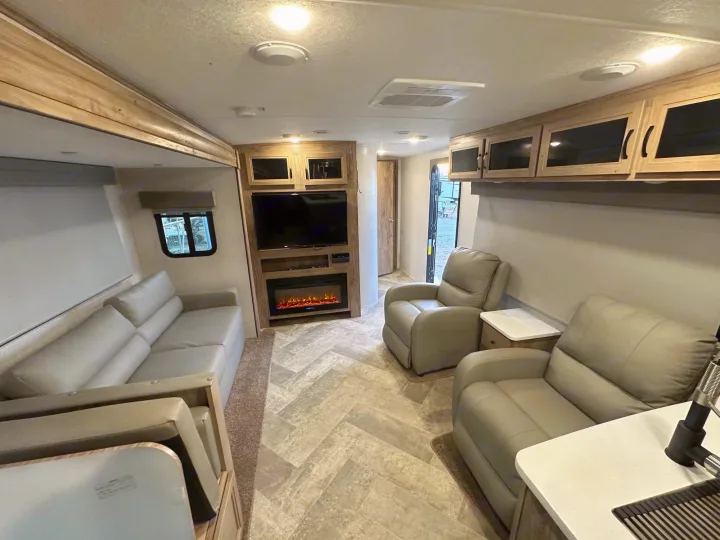 Spacious RV rental living area, featuring a sofa, two recliners, a TV, fireplace, and a partial kitchen counter in a modern, comfortable interior.. Palomino Salaire Ultralite 2022